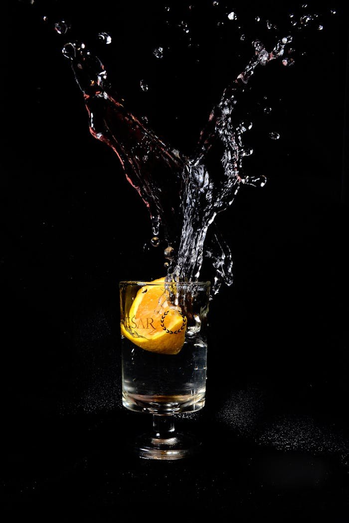 Dynamic splash of liquid with lemon in a glass on a black background.
