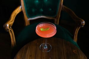A stylish pink cocktail garnished with a lime slice sits elegantly on a wooden table.
